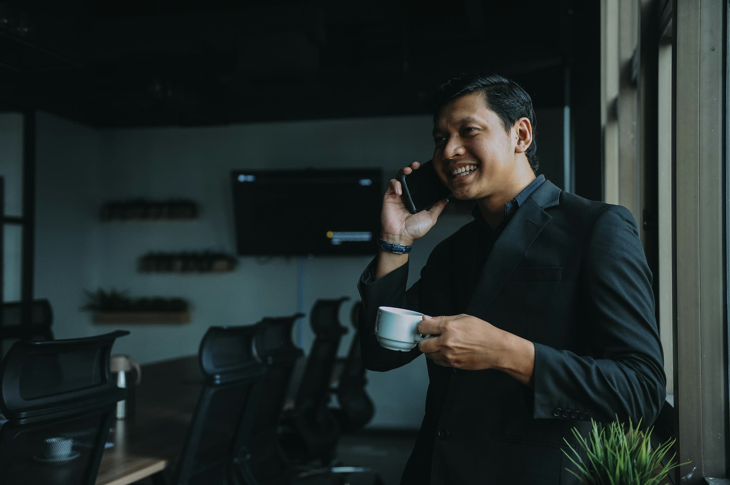 A smiling professional on a phone call holding a coffee in a modern office