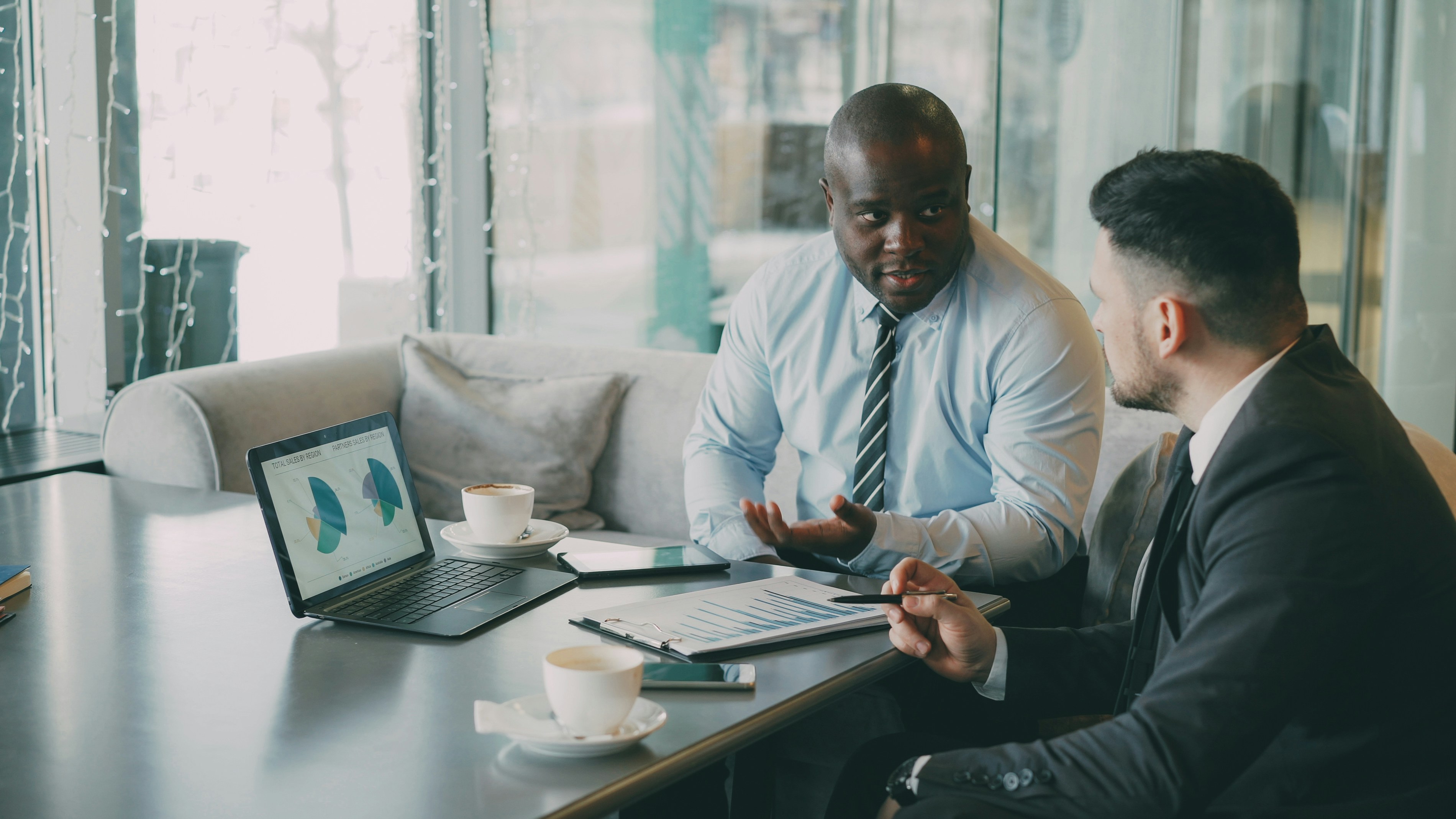 Two businessmen in a modern glass office reviewing a financial chart together